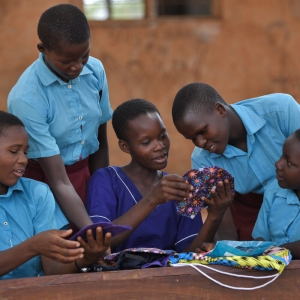 four  girls in blue tops showing each ther their menstrual packs sewing projects. 
